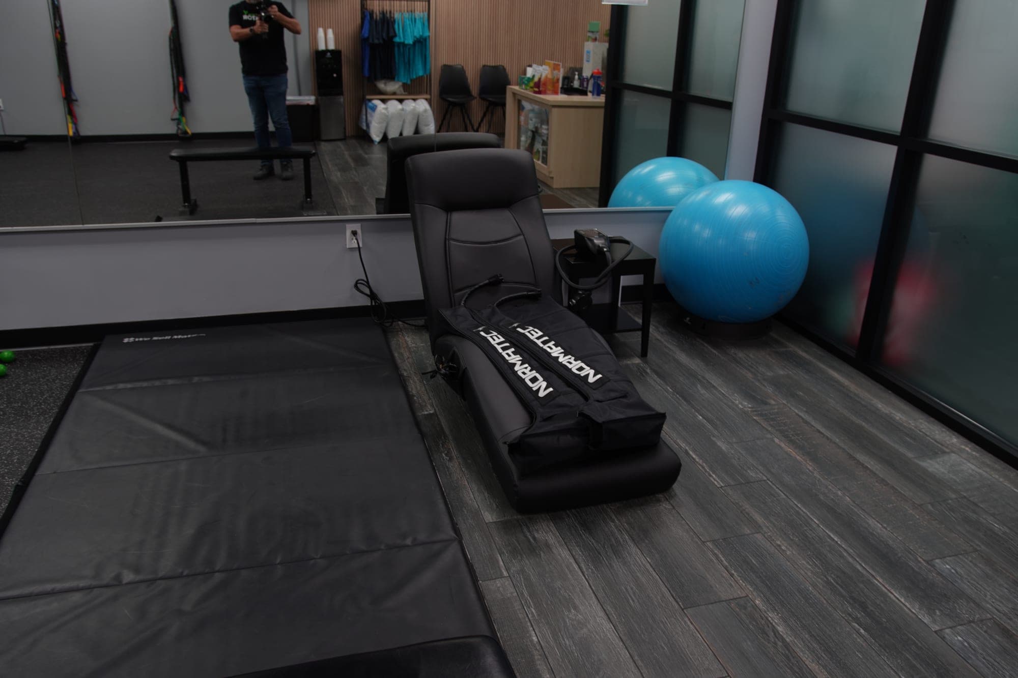 Normatec compression recovery chair in the rehab area, with exercise mats, stability balls, and resistance bands nearby